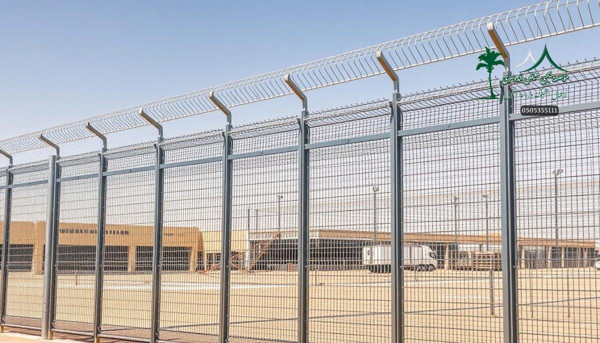 A high-quality metal mesh fence system stands tall, its sleek silver finish gleaming in the warm desert sun. Skilled workers carefully install the durable panels, ensuring a secure and long-lasting perimeter. The fence's intricate design features clean lines and precise geometric patterns, blending seamlessly with the contemporary architecture of the Riyadh cityscape. Robust steel posts anchor the mesh firmly, providing uncompromising protection while maintaining an elegant, minimalist aesthetic. Carefully considered lighting casts dramatic shadows, accentuating the fence's sophisticated style and emphasizing its crucial role in safeguarding this modern urban landscape.